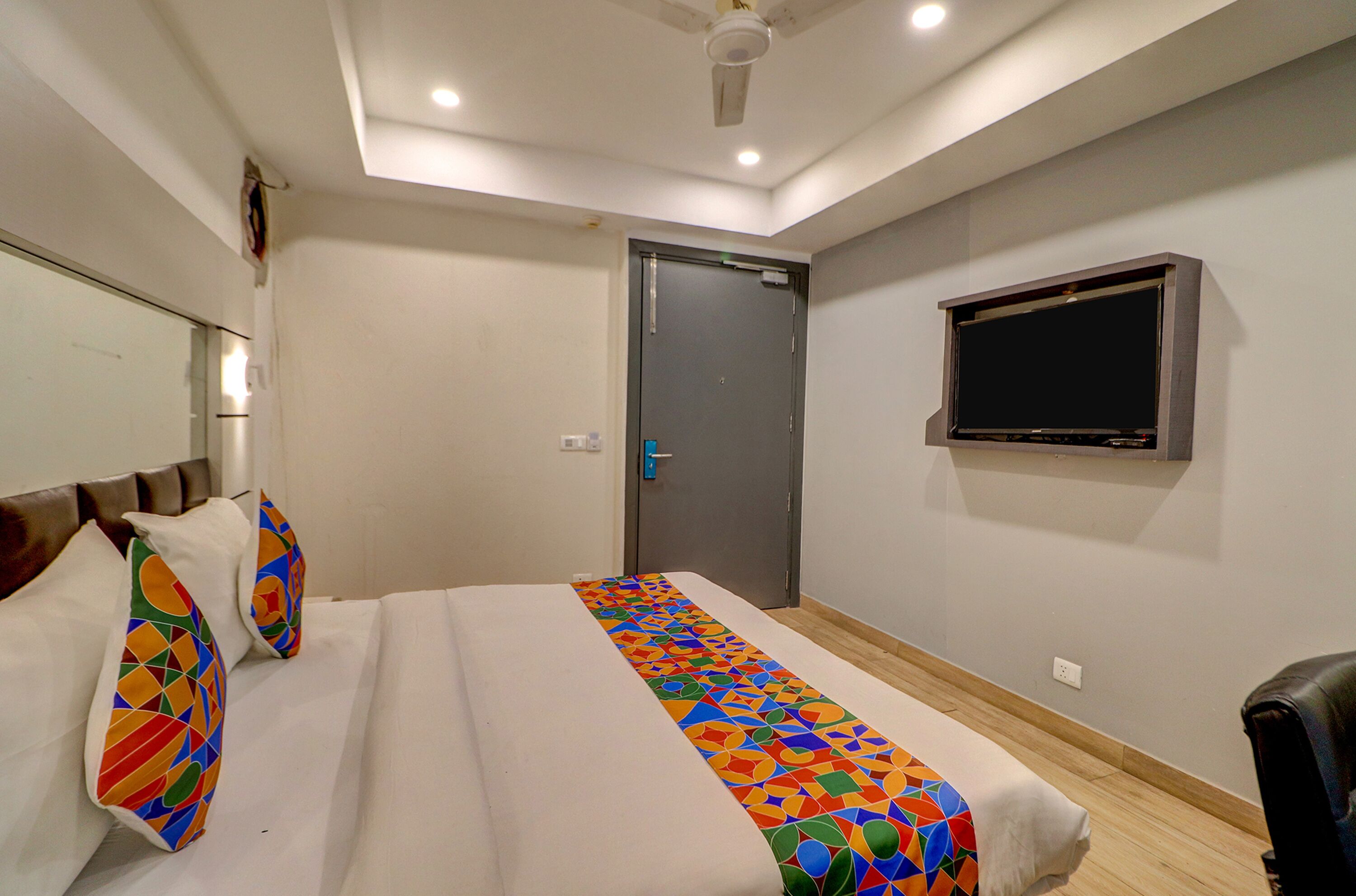 Quarto de hotel com cama, televisão, porta e ventoinha no teto.