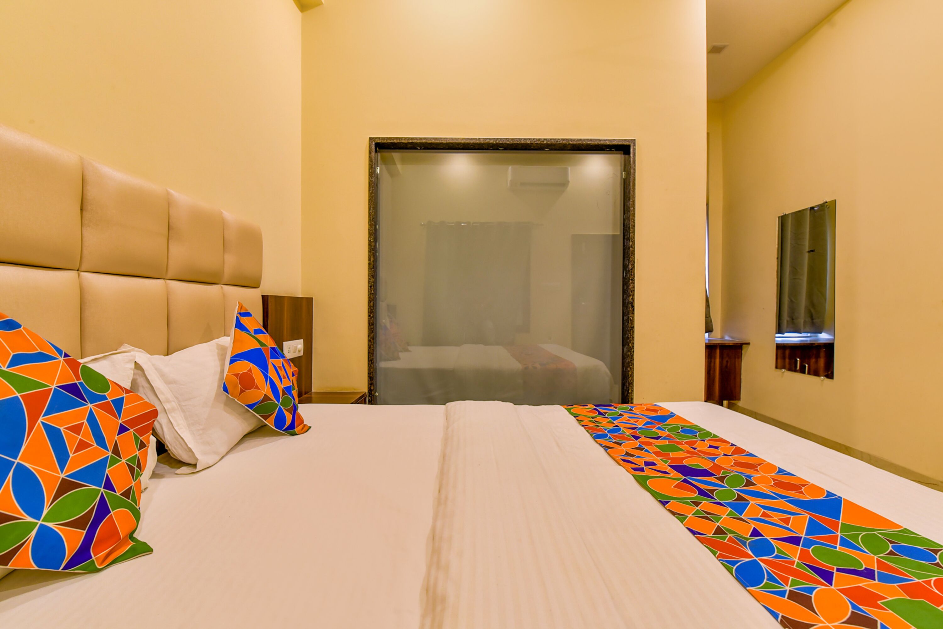 Hotelkamer met een groot bed, hoofdeinde, spiegel en een deur met een geëtste ruit.