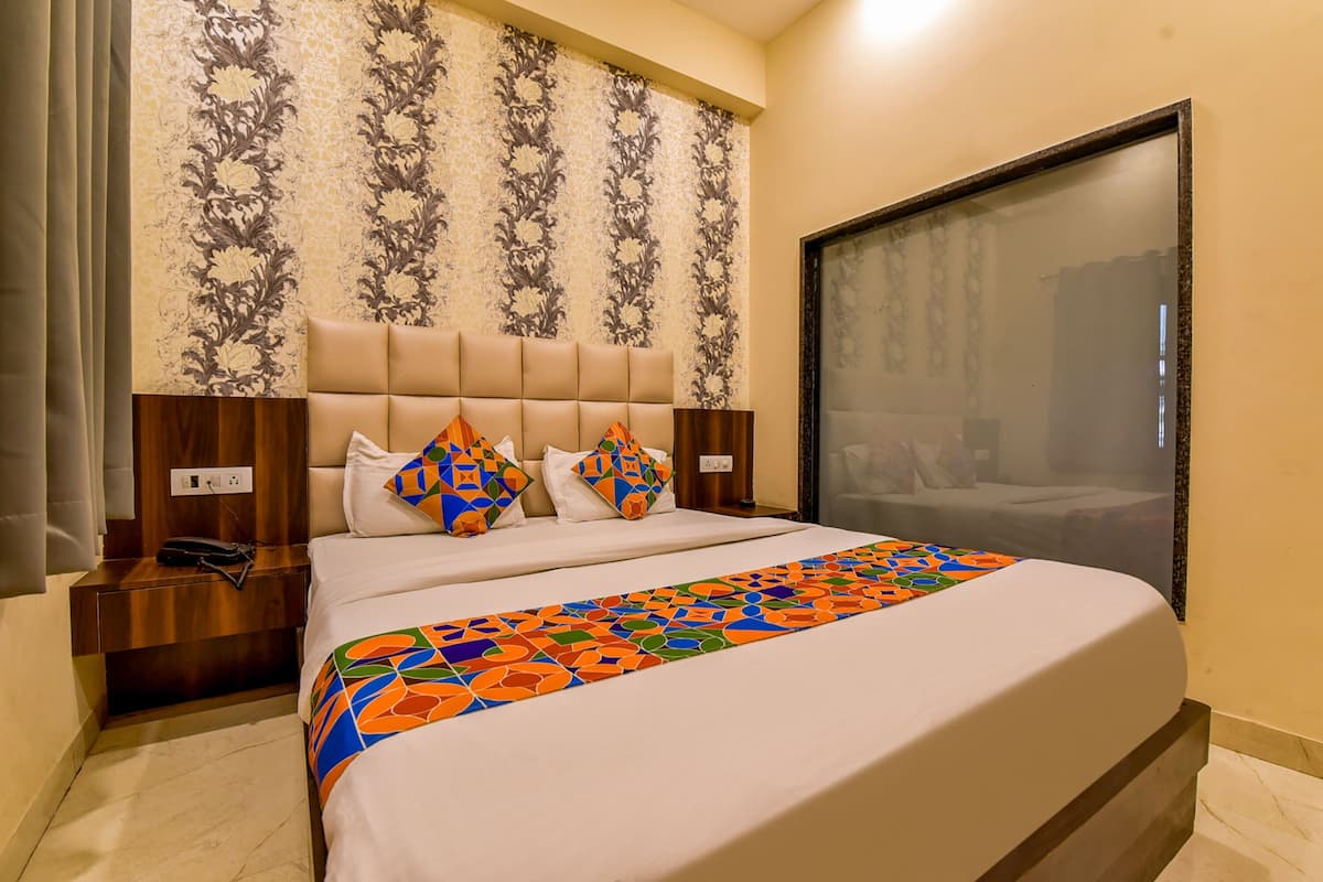 A hotel room with a large bed, a headboard with a floral pattern, a nightstand with a phone, and a window with a view.