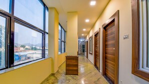 Un pasillo con amplios ventanales, puertas de madera y suelo de mármol.