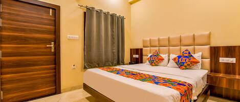 A hotel room with a wooden door, a bed with a colorful bedspread, a headboard, and a nightstand.