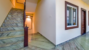 Una escalera con escalones de mármol y barandillas de madera, que conduce a un rellano con una lámpara.
