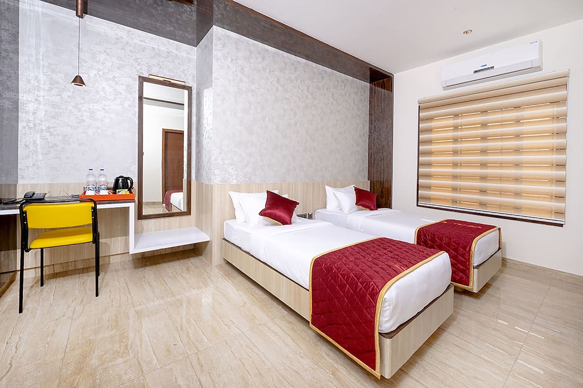 A hotel room with two beds, a desk with a chair, a mirror, and a window with blinds.