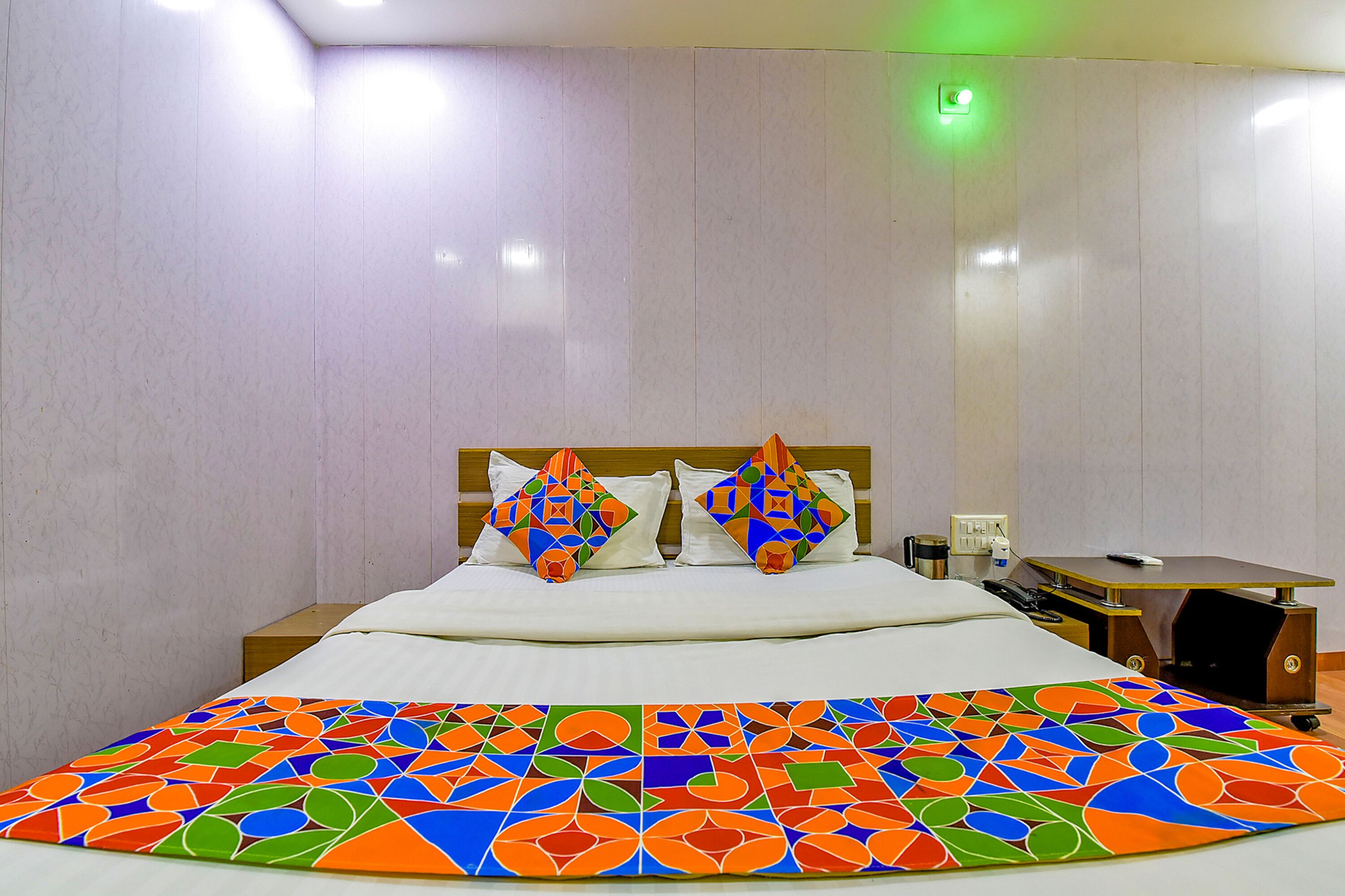 A hotel room with a bed, two pillows, a desk, and a chair.