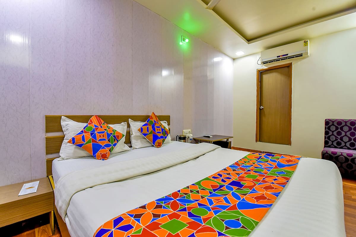 A hotel room with a large bed, a nightstand, a desk, an air conditioning unit, and a door.
