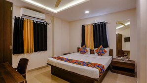 Habitación de hotel con cama, escritorio, silla, aire acondicionado, cortinas, ventilador de techo y espejo.