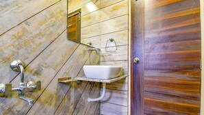 Un baño con piso de madera, un lavamanos blanco sobre una repisa y una puerta con panel de madera.