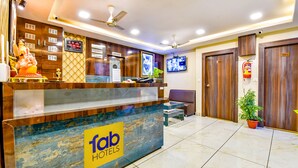 Zona de recepción de un hotel con mostrador, televisor, ventilador de techo y extintor.