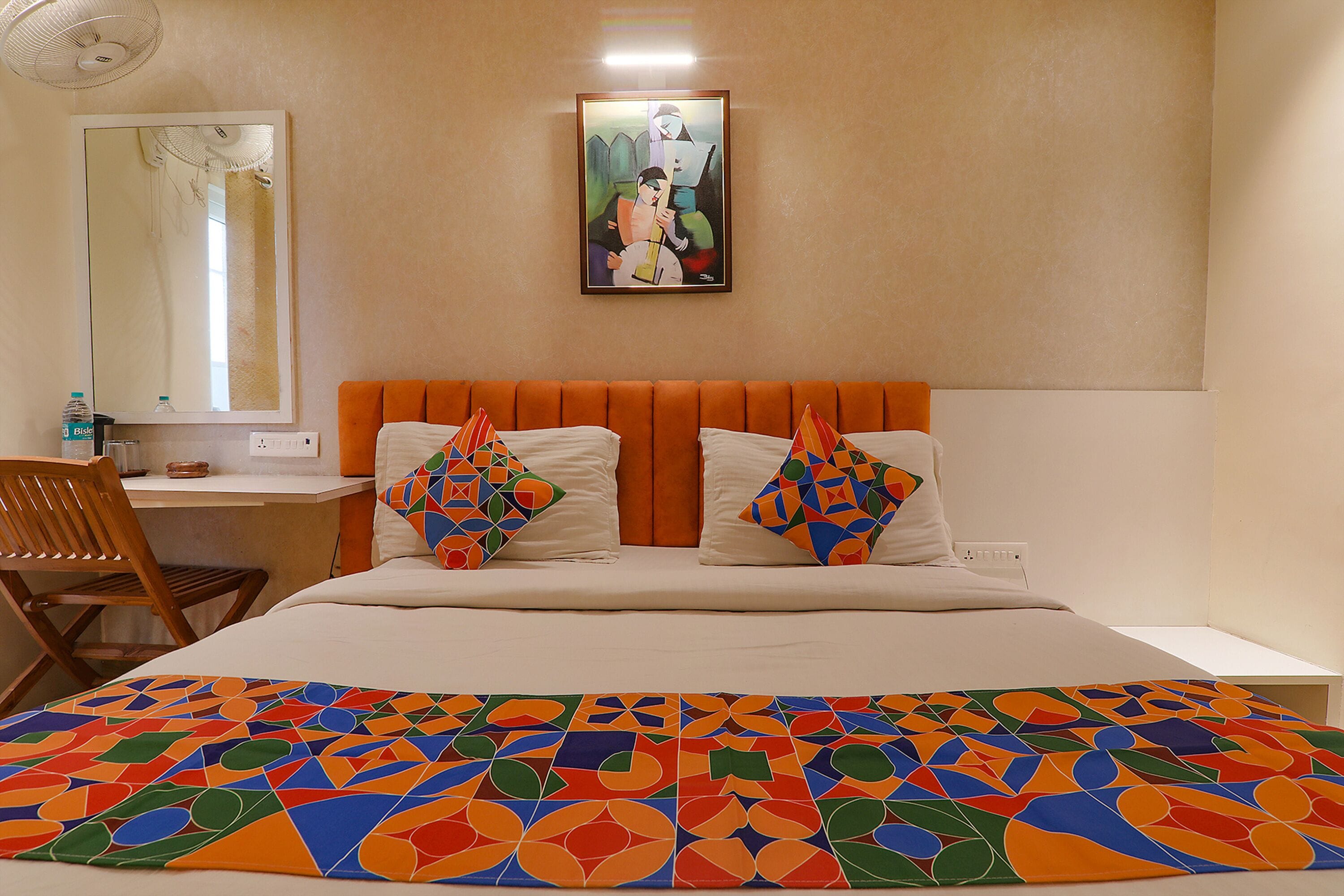 A hotel room with a bed, a desk, a chair, and a painting on the wall.