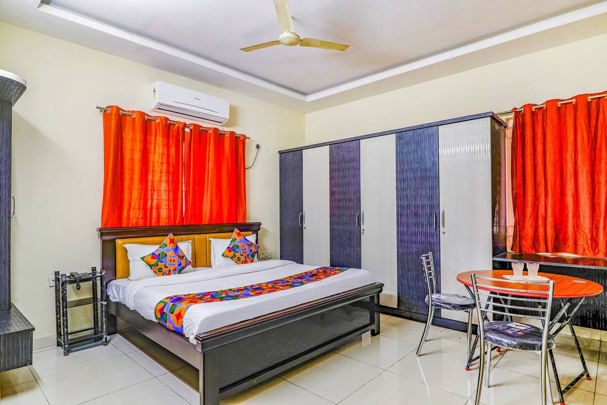 A hotel room with a bed, a desk, and a chair. There is a wardrobe, a ceiling fan, and an air conditioning unit.