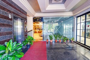 A hotel reception area with a red carpet, potted plants, and a reception desk.