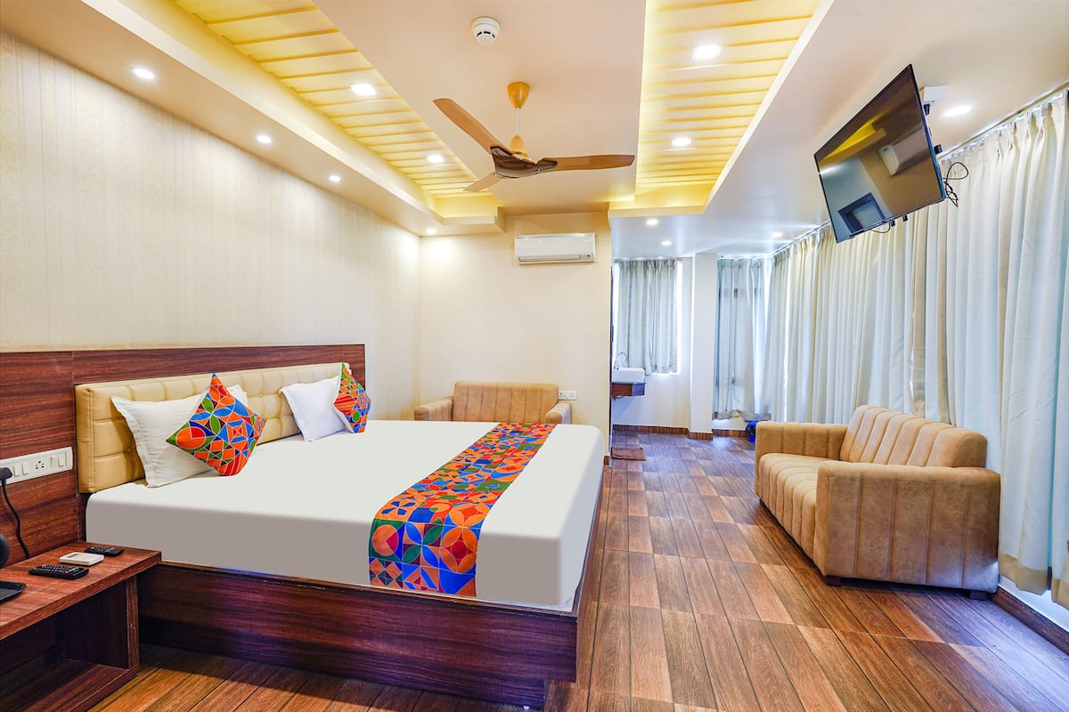 Una habitación de hotel con una cama, un sofá, un televisor montado en la pared y un ventilador de techo.
