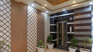 A modern hotel lobby with a geometric patterned wall, a glass elevator, and potted plants. - FabHotel Super 3 Premium - 800m from Kashi Vishwanath Temple (Varanasi)