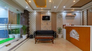 A reception area with a wooden reception desk, a black sofa, and a glass partition. - FabHotel Super 3 Premium - 800m from Kashi Vishwanath Temple (Varanasi)