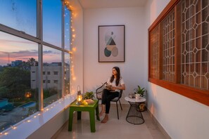 Una habitación con un ventanal amplio, una mesita con un farol y una silla.