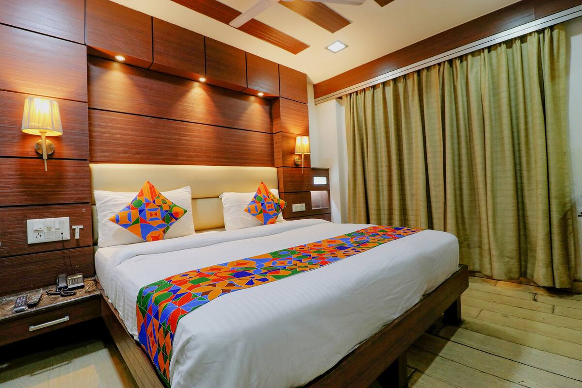 A hotel room with a large bed, wooden headboard, two bedside lamps, a telephone, and a window with curtains.