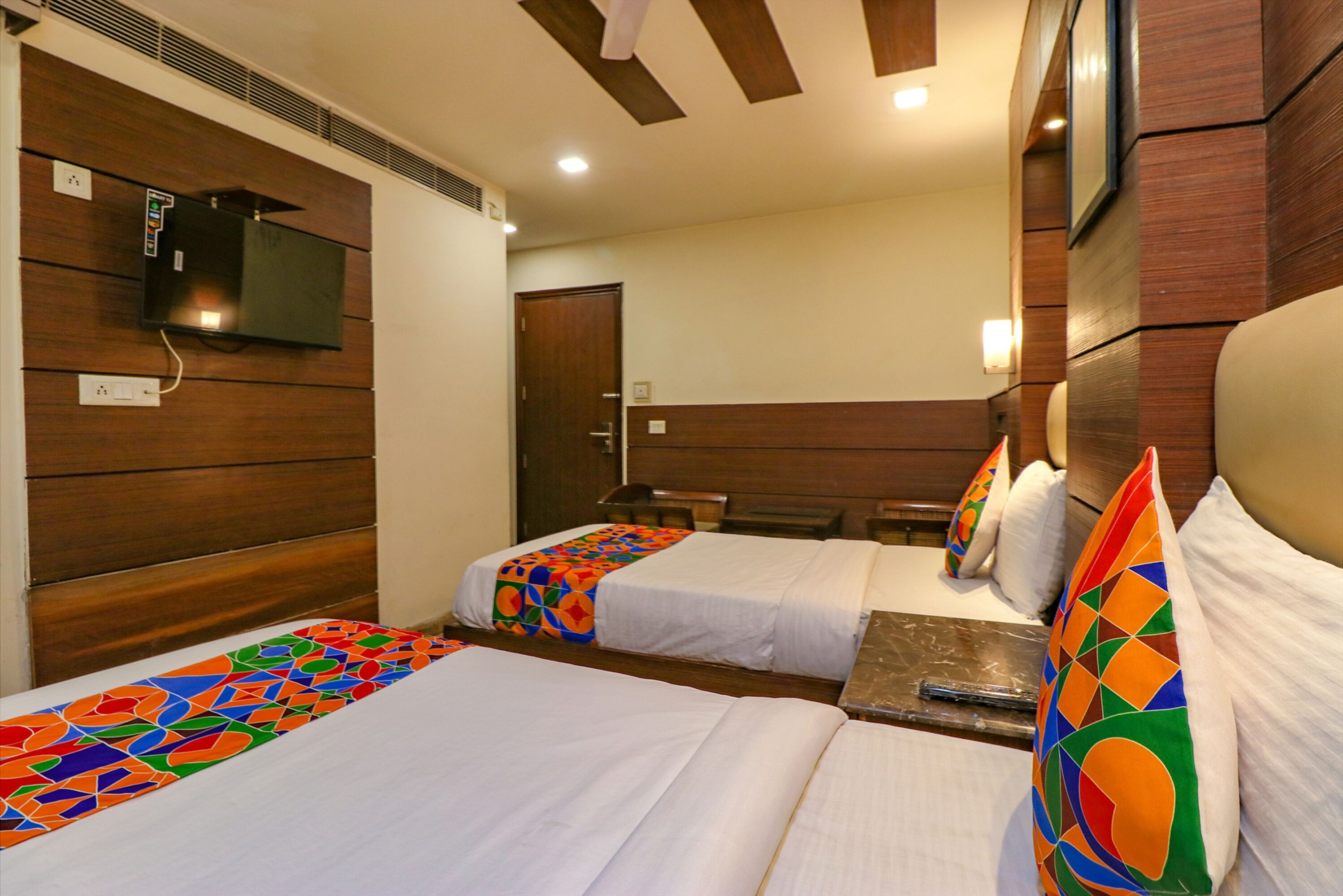A hotel room with two beds, a TV mounted on the wall, and a wooden headboard.