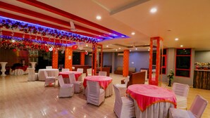 A banquet hall with round tables covered in white tablecloths and red centerpieces, surrounded by white chairs. - FabHotel A One Noida Sector 11 (Noida)