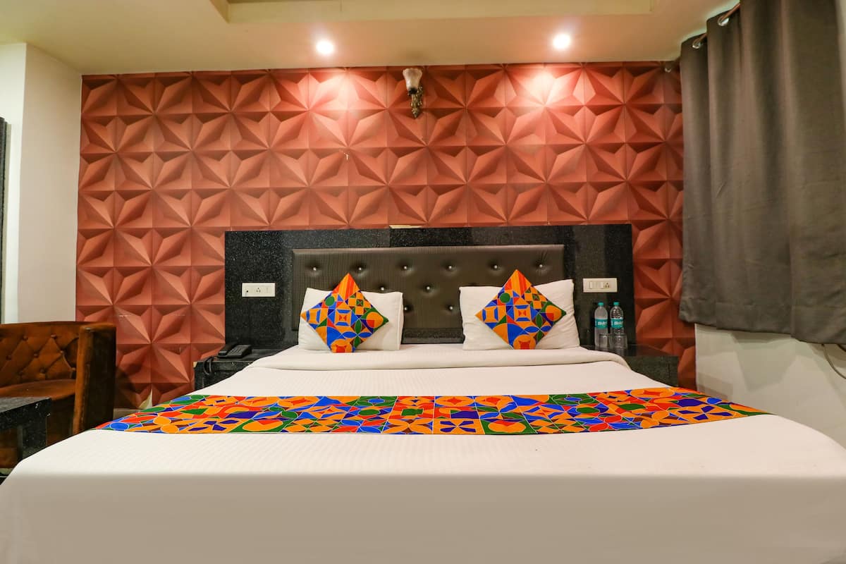 Quarto de hotel com parede de padrão geométrico, cabeceira estofada, cobre-leito colorido e cortina marrom.