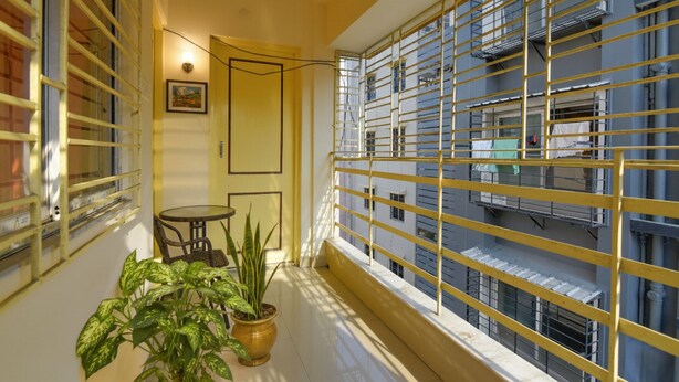 A narrow balcony with yellow metal bars, a potted plant, a small round table, and a chair. - Fabhotel Capital Casa (Barasat)