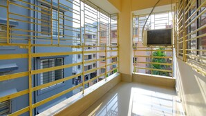 A balcony with yellow metal railings, a view of neighboring buildings, and a window with an air conditioning unit. - Fabhotel Capital Casa (Barasat)