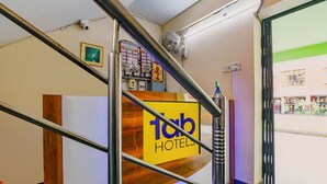 A hotel reception area with a wooden reception desk, a sign reading "Tab Hotels," and a staircase with metal railings. - Fabhotel Capital Casa (Barasat)