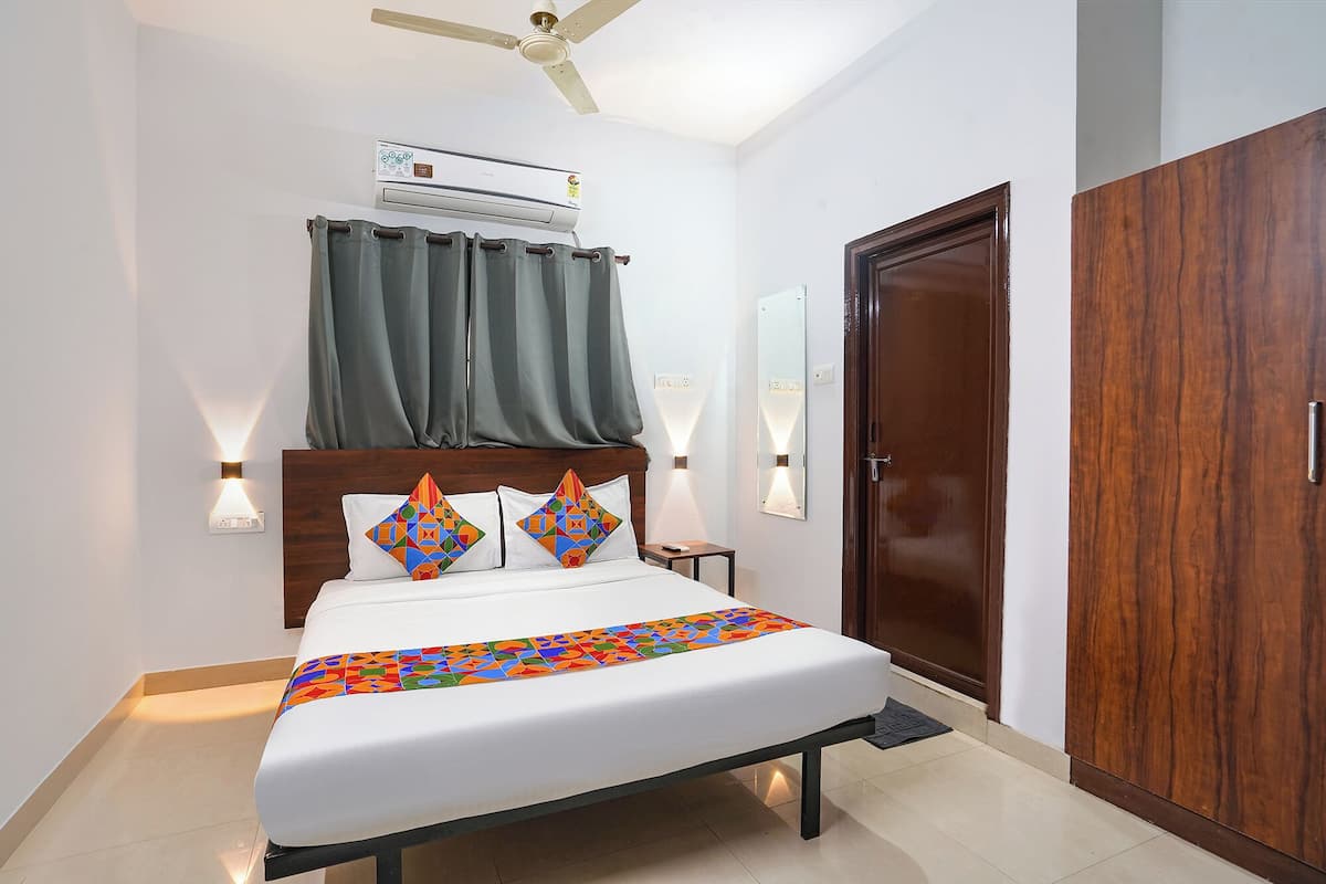 A neatly arranged hotel room with a bed, a ceiling fan, an air conditioning unit, a wardrobe, and two wall-mounted lights.