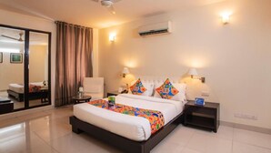 A hotel room with a large bed, two bedside tables, a ceiling fan, an air conditioning unit, and a sliding glass door leading to a balcony. - Fabhotel Anutham (New Delhi)