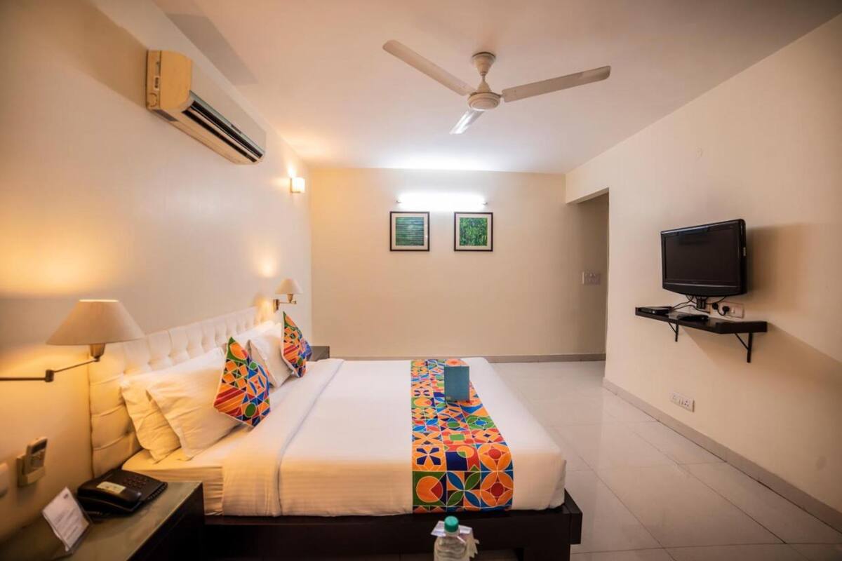 A hotel room with a bed, a TV mounted on the wall, a ceiling fan, and two framed pictures on the wall.
