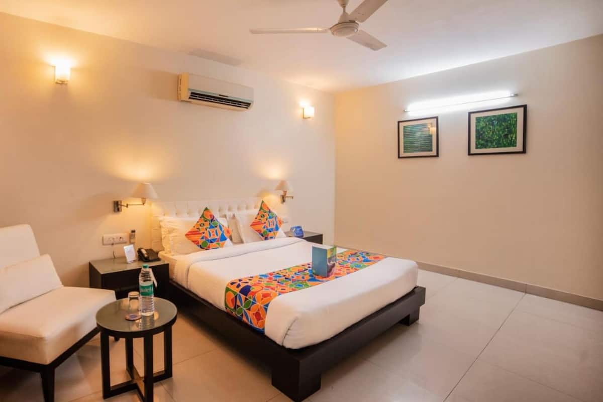 A hotel room with a bed, a chair, a small table, and a ceiling fan.