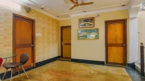 Un vestíbulo de hotel con puertas de madera, un ventilador de techo, piso de mármol y una pequeña mesa con una silla.