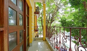A balcony with a yellow railing, a wooden door, and a view of trees. - FabExpress Elite Stay I (Barasat)