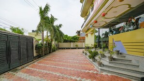 A paved walkway leading to a building with a yellow facade and a staircase with potted plants. - Fabhotel Kriti Green (Varanasi)