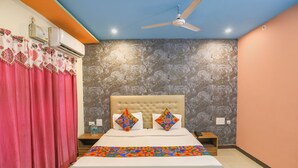 A bedroom with a tufted headboard, a bed with patterned pillows, a ceiling fan, and a decorative wall. - Fabhotel Kriti Green (Varanasi)