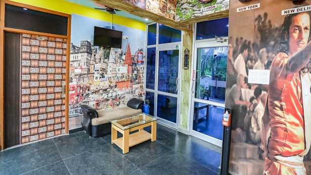 A lobby with a glass coffee table, a sofa, a wall with clocks and a poster, and a door with a numbered panel. - Fabhotel Kriti Green (Varanasi)
