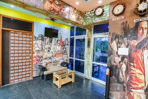 A lobby with a glass coffee table, a sofa, a wall with clocks and a poster, and a door with a numbered panel. - Fabhotel Kriti Green (Varanasi)