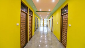 A long, narrow hallway with bright yellow walls and a shiny floor, leading to a bright room with a large window. - Fabhotel Kriti Green (Varanasi)