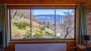 Een kamer met een groot raam dat uitzicht biedt op een heuvellandschap en een meer.