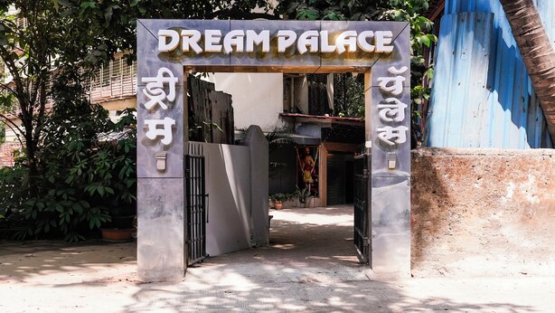 Una entrada cerrada con letrero que dice 'DREAM PALACE', una reja metálica y una planta en maceta.