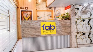 Una recepción con encimera de mármol, un letrero de 'fab hotels', un reloj y una planta.