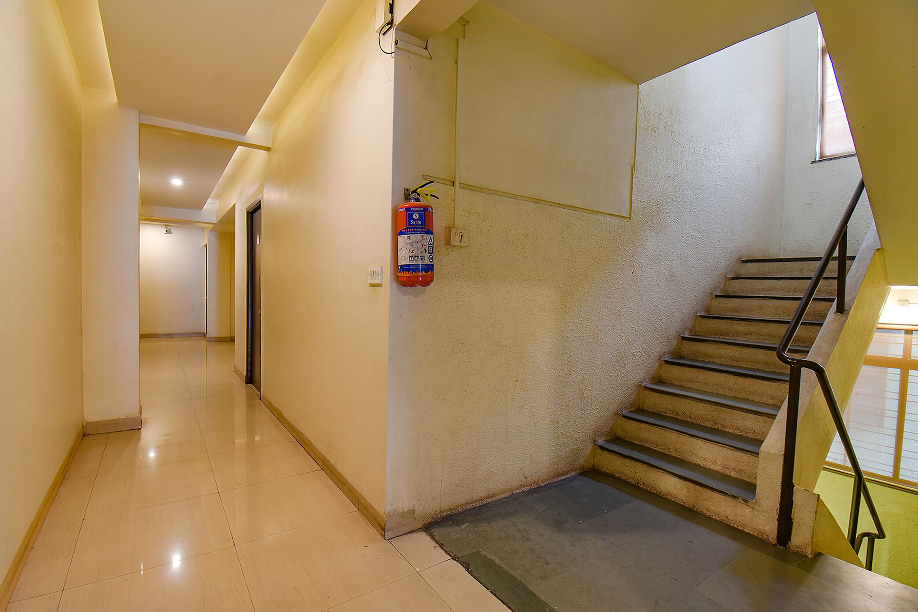 Un couloir propre et bien éclairé, avec un extincteur fixé au mur, un escalier doté d’une rampe métallique et une porte au bout du couloir.