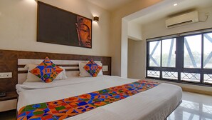 A modern hotel room with a large bed, a colorful throw blanket, and a large window with a view of a bridge. - FabHotel Royce Studio (Pune)