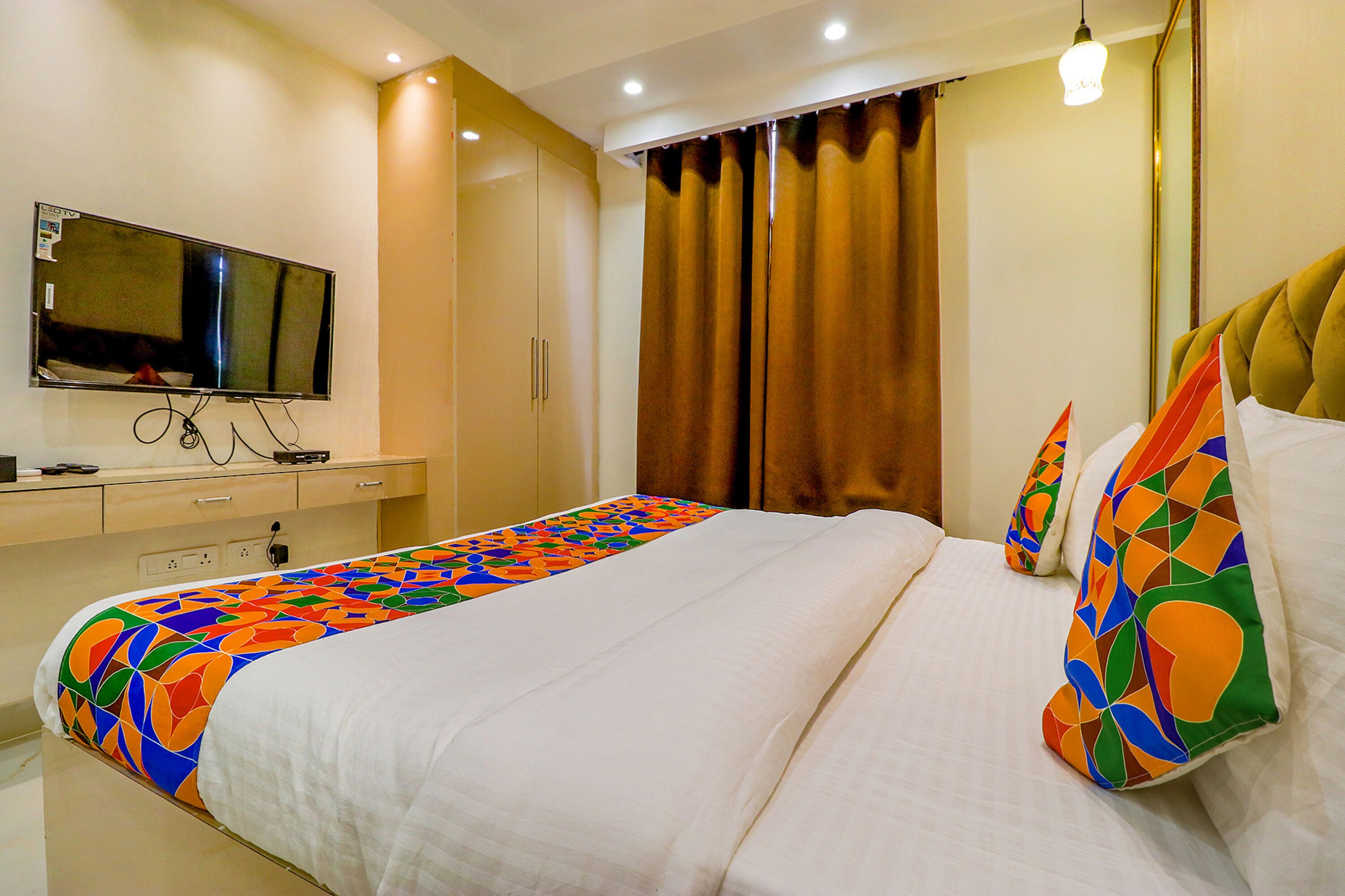 Une chambre d’hôtel moderne avec un lit bien fait, un téléviseur à écran plat fixé au mur et une grande fenêtre avec des rideaux.