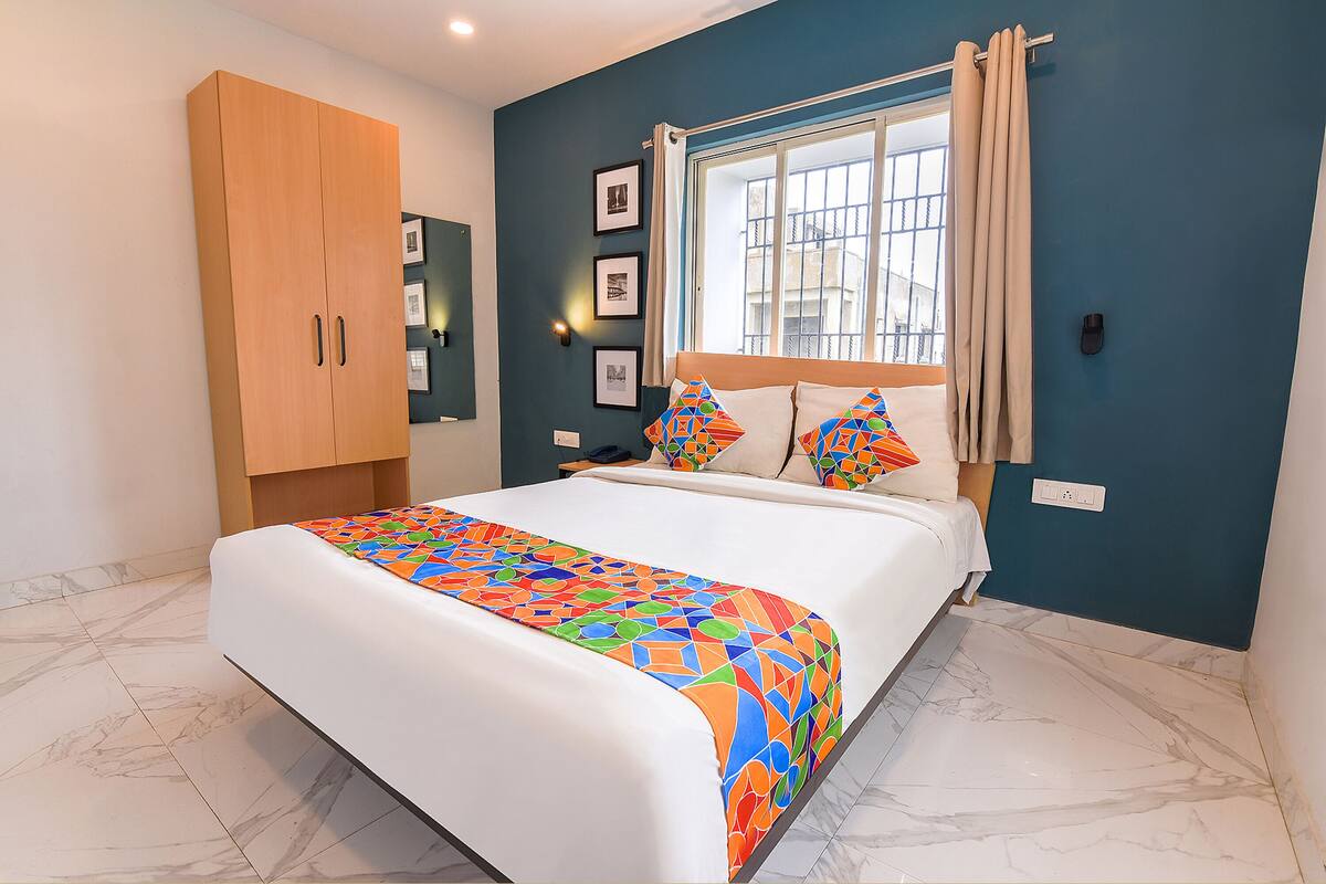 A bedroom with a bed, a wardrobe, a window with curtains, and framed pictures on the wall.