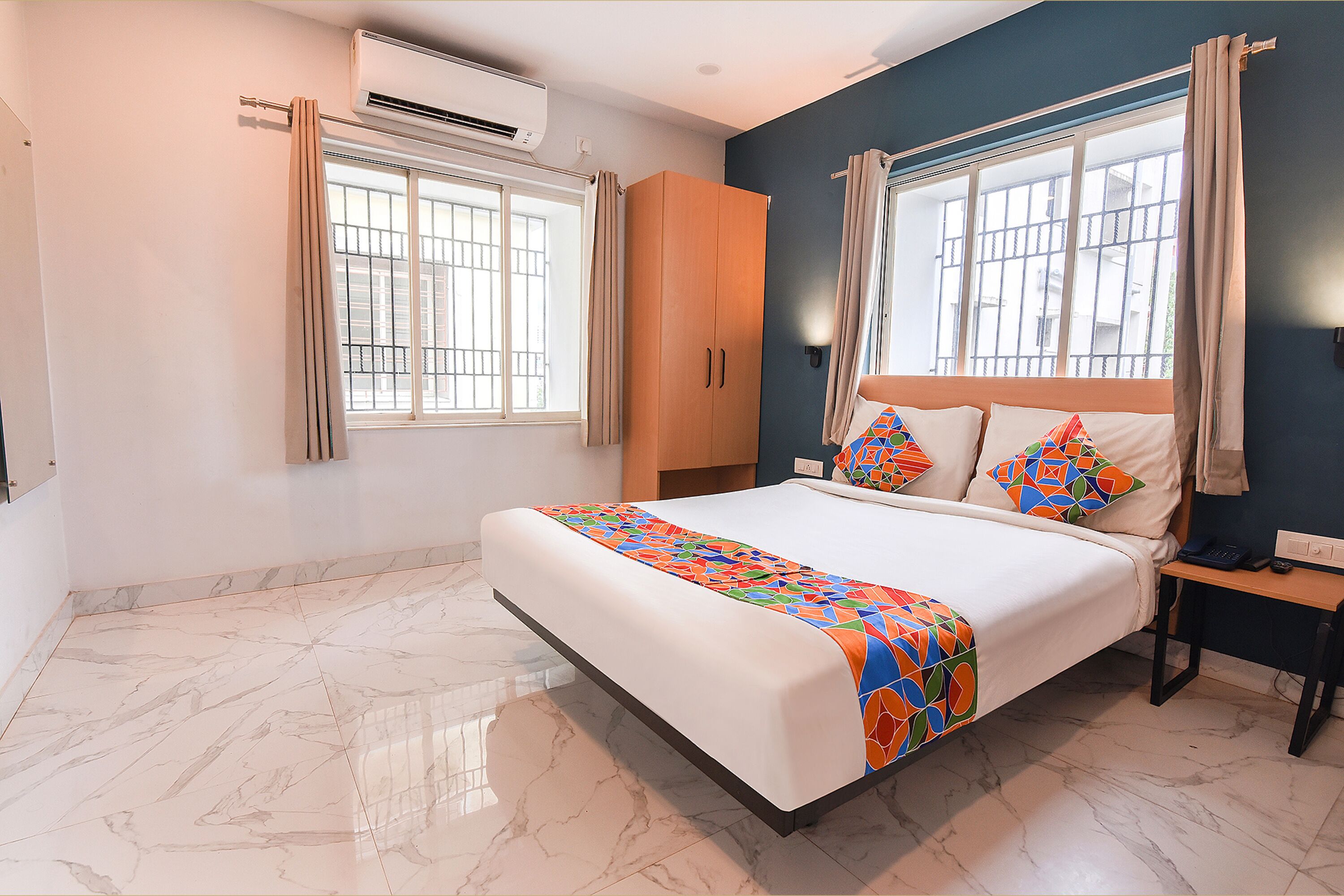 A bedroom with a bed, a nightstand, an air conditioner, and a window with curtains.