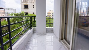 A balcony with a metal railing, a white floor, and a view of buildings and greenery. - Fabhotel Eden (Baruipur)