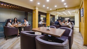 A modern dining area with round tables and cushioned seating, featuring a central floral arrangement. - Fabhotel Sr Wakad (Paud)