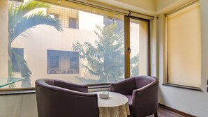 A room with a round table and two chairs, a window with a view of buildings and trees, and a door with a handle. - Fabhotel Sr Wakad (Paud)