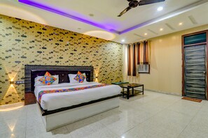 A hotel room with a large bed, a ceiling fan, a small table, and a door with a window. - Fabhotel Gold Galaxy (Kanpur)