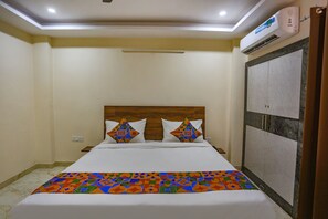 A hotel room with a bed, a headboard, a wardrobe, and an air conditioning unit.